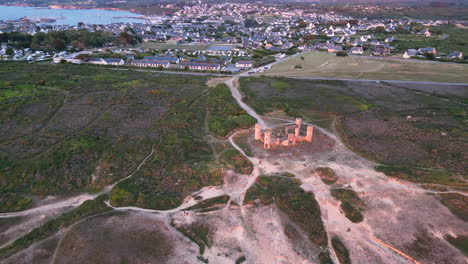 tilt upward aerial view of a city beyond a hill with pathways running through around an abandoned mansion