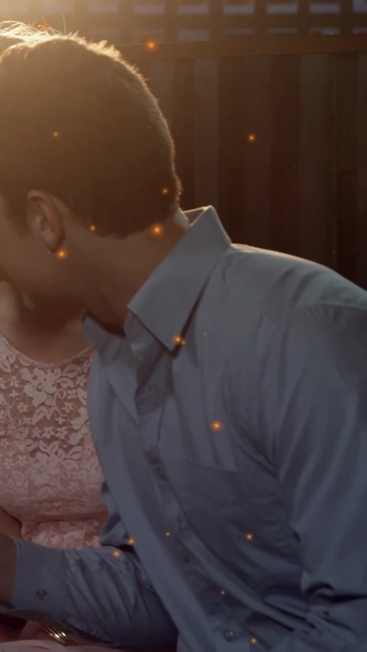Vertical video: Man turning head leaning toward woman on bench, showing phone amid glow for ads