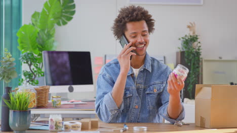 Hombre-Que-Dirige-Un-Negocio-En-Línea-Haciendo-Velas-Boutique-En-Casa-Hablando-Por-Teléfono-Móvil