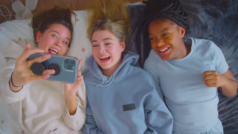 group of smiling multi-cultural teenage girl friends posing for selfie on mobile phone at home