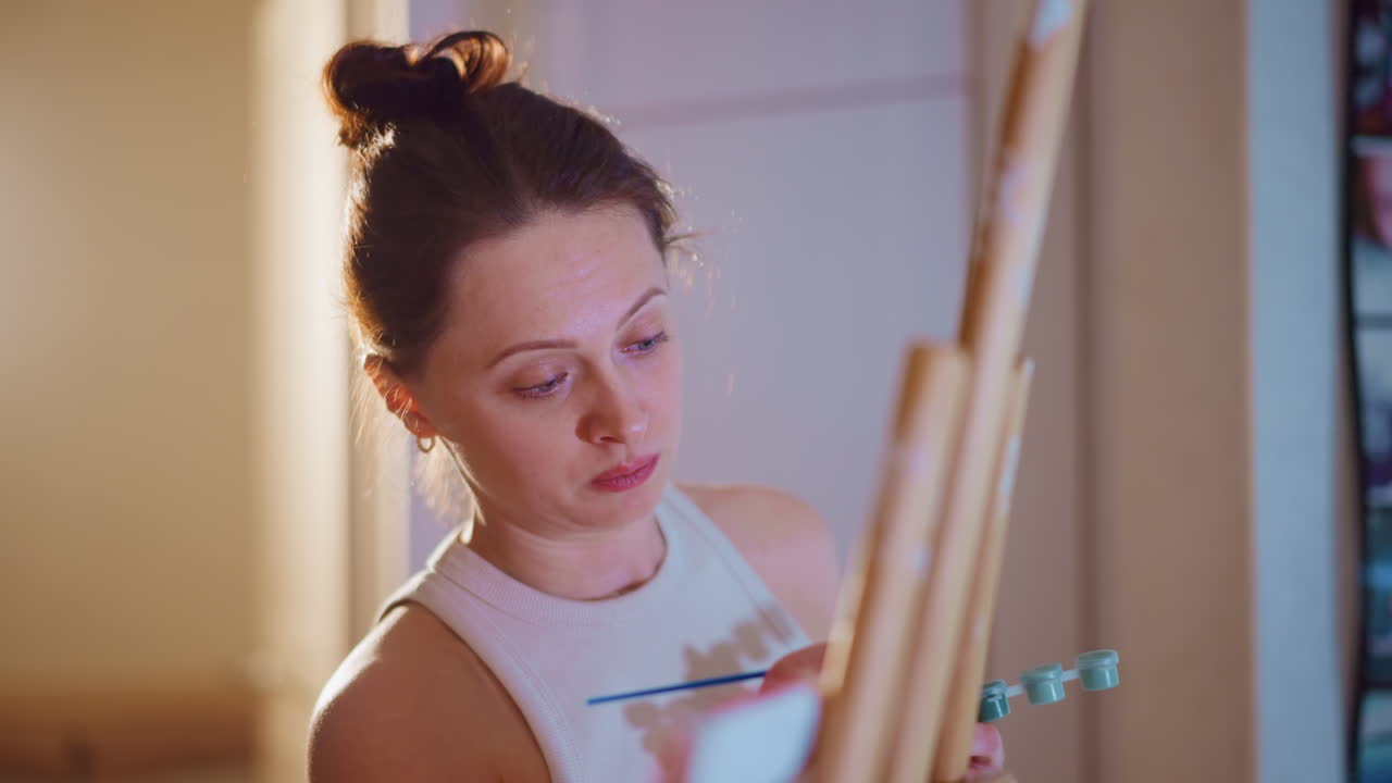 Young White Woman Mixing Colors On Palette In Focused CloseUp, Art Student Exploring Tone And Hue, Careful Brushwork, Soft Evening Lamp Behind, Attentive Expression And Precise Technique