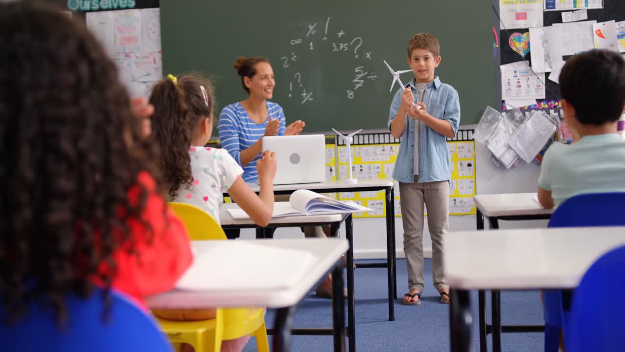 Pohled zepředu na bělošského školáka vysvětlujícího model větrného mlýna ve třídě 4K.