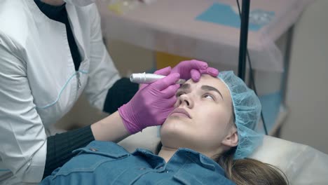 las manos de la esteticista con guantes rosados aplican maquillaje permanente