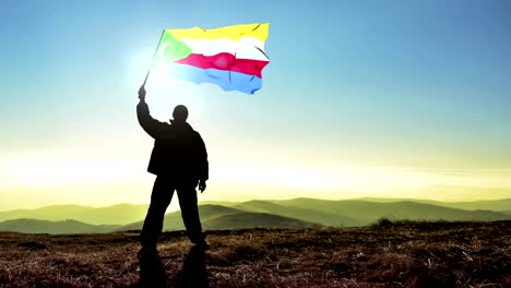 exitoso hombre silueta ganador agitando bandera de las comoras en la parte superior del pico de la montaña. fondo de bucle cinemagraph