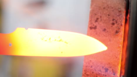 cuchillo rojo ardiente que se retira del horno listo para ser forjado con llamas de fuego escapando de la entrada del horno caliente con fondo borroso