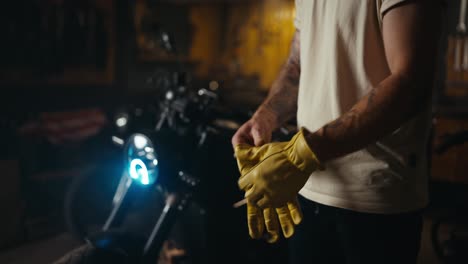 cerca de un tipo en una camiseta blanca poniendo guantes amarillos mientras comienza su día de trabajo en un taller de motocicletas