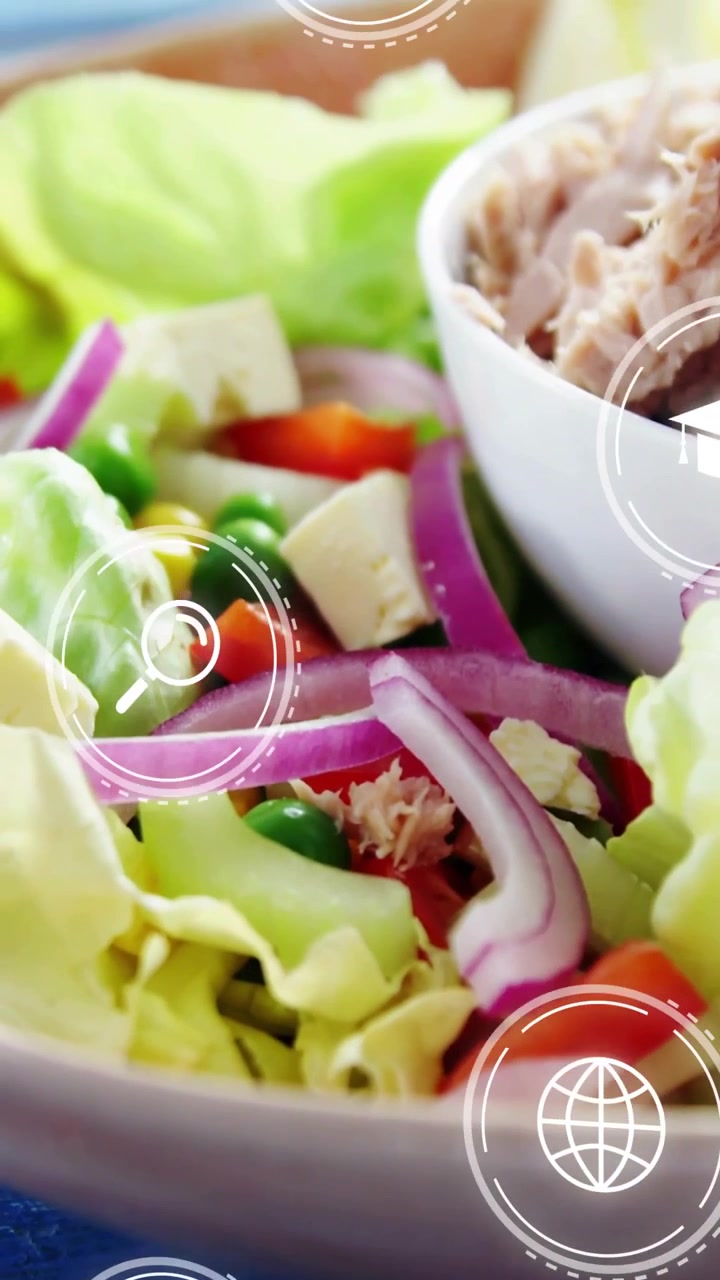 Vídeo vertical: Câmera afastando-se de uma borda em macro, revelando uma salada, ícones flutuantes sobre uma mesa azul