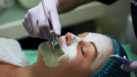 covering caucasian woman's face with white mask. cosmetology procedures at beauty salon. close up.