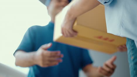 close up parcel in hand of blue uniform delivery man to customer front of the house from shopping online with good service. courier man delivering a cardboard box postal package to destination.