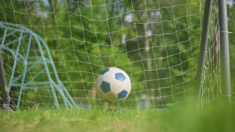 a soccer ball is kicked into a goal post on a grassy field, then gently rolls out towards the camera