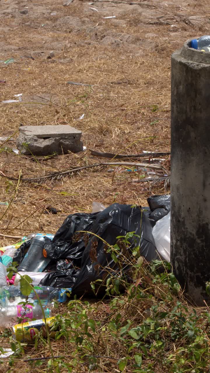 Una lenta panoramica rivela bottiglie di plastica abbandonate e sacchi neri della spazzatura sull'erba secca.