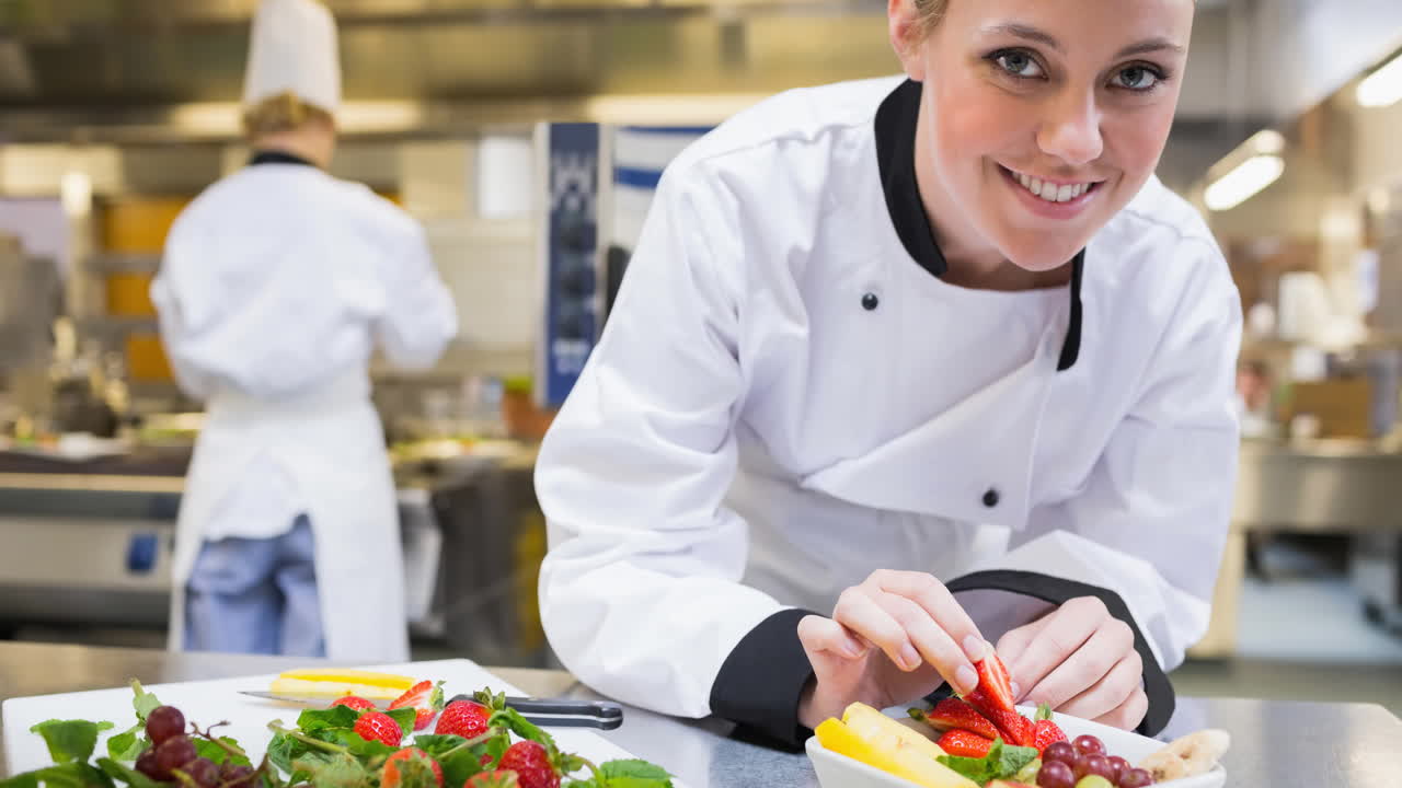 una chef caucásica sonriente con un delantal preparando comida en una cocina profesional