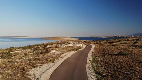 Female-runner-approaching-on-the-road-from-the-distance-in-the-early-morning,-with-sea-in-the-background