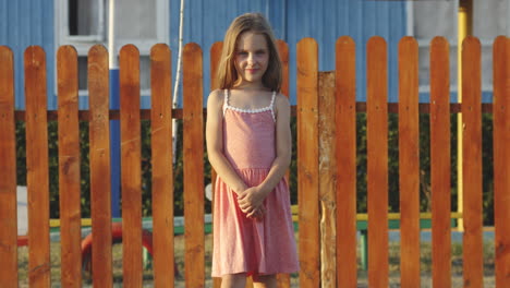 girl in pink dress standing by a colorful fence