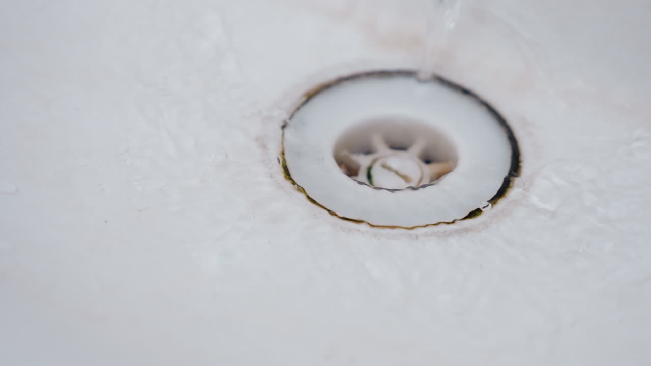 Overhead bathtub drain with blackened ring and mineral discoloration cleaning technician or service inspects drain, evaluates grime and limescale, prepares tools for scrub and rinse, neutral daylight