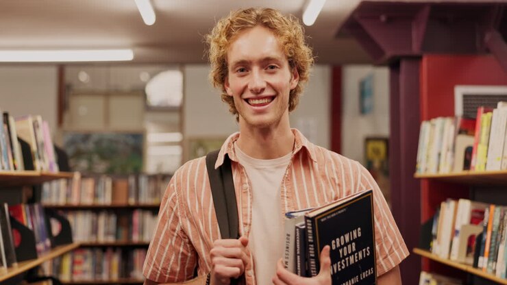 Uno studente sorride in biblioteca con libri in mano
