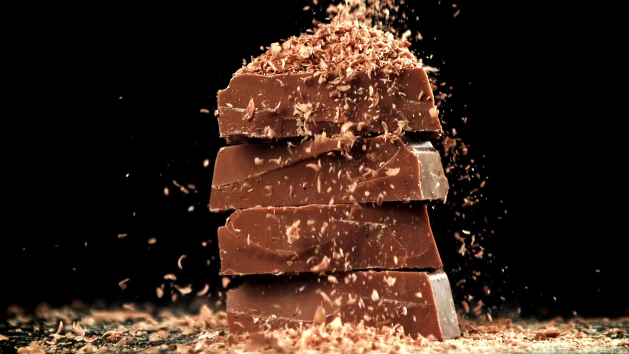 Caduta al rallentatore di scaglie di cioccolato su tavolette di cioccolato impilate