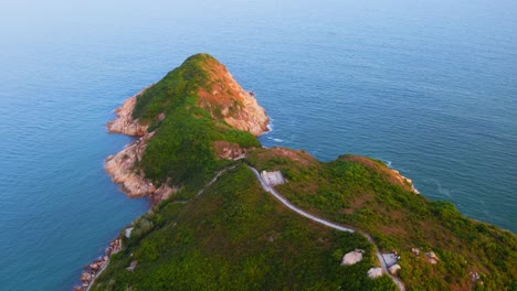 drone shot traveling forward above a small island with hills and vegetation toward the sea during the day