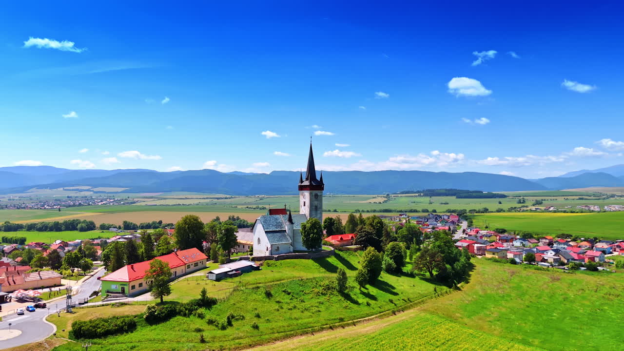 Village church in countryside. A picturesque village features a prominent church amidst rolling hills and lush greenery under a clear blue sky