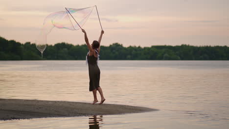 a young girl artist shows magic tricks using huge soap bubbles. create soap bubbles using sticks and rope at sunset to show a theatrical circus show