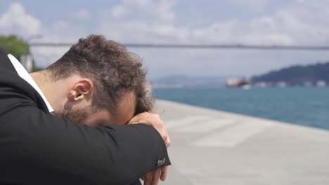 sad businessman by the sea. he puts his head in front of him.