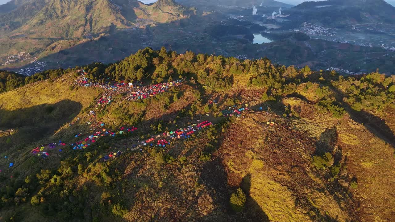Aerial view hundreds of campers gather on a scenic highland ridge. Hiker tents illuminated under the soft sunrise sky. Sunrise camp point of Mount Prau, Indonesia