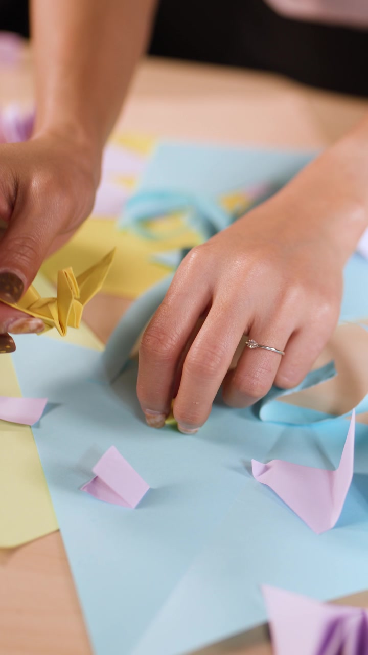 Una persona piega con cura carta gialla e blu in forme di origami su un tavolo di legno.