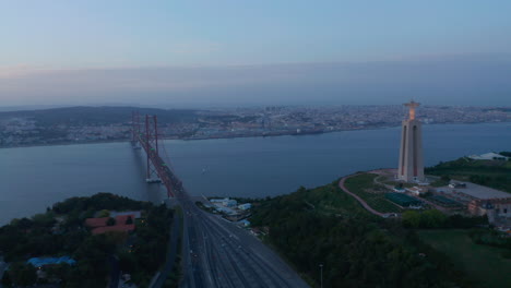 Breiter-Panoramablick-Auf-Die-Küste-Von-Lissabon-Mit-Dem-Stadtzentrum,-Dem-Denkmal-Des-Schreins-Von-Christ-Rei-Und-Dem-Autoverkehr-über-Die-Rote-Brücke-Brücke-Des-25.-April