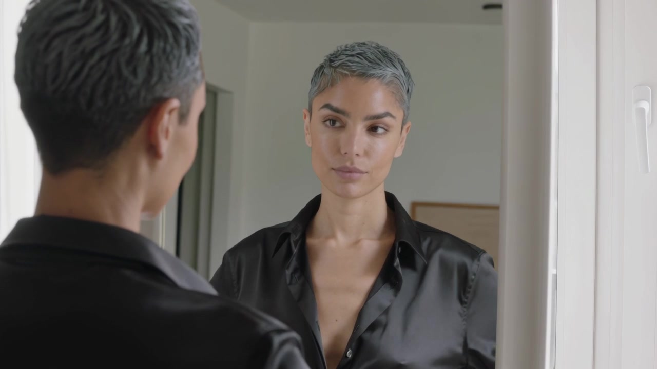 Vedendo il riflesso, donna che si sistema i capelli, rimbocca la camicia nera, controlla il taglio di capelli allo specchio di casa.