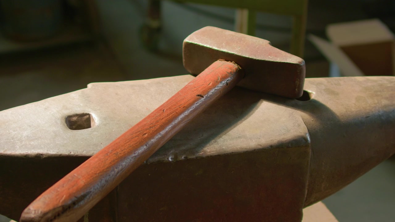 Marteau de forgeron et enclume, faisceau de lumière chaude illuminant les outils d'atelier, prise de vue à main levée. Gros plan sur l'équipement de métallurgie traditionnelle sur l'acier de forge.