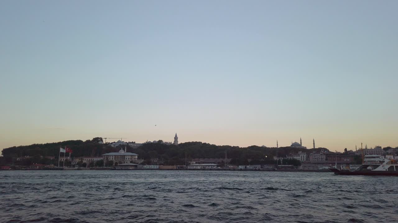 noche, cinematográfico en cámara lenta, la vista desde un ferry que navega a lo largo del bósforo en estambul, mostrando los árboles y el telón de fondo icónico de hagia sophia y el paisaje urbano de estambul