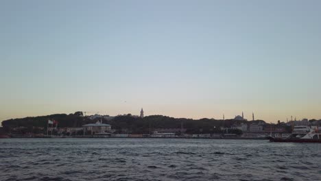 evening, cinematic slow-mo, the view from a ferry sailing along the bosphorus in istanbul, showcasing the trees and the iconic backdrop of hagia sophia and the istanbul cityscape