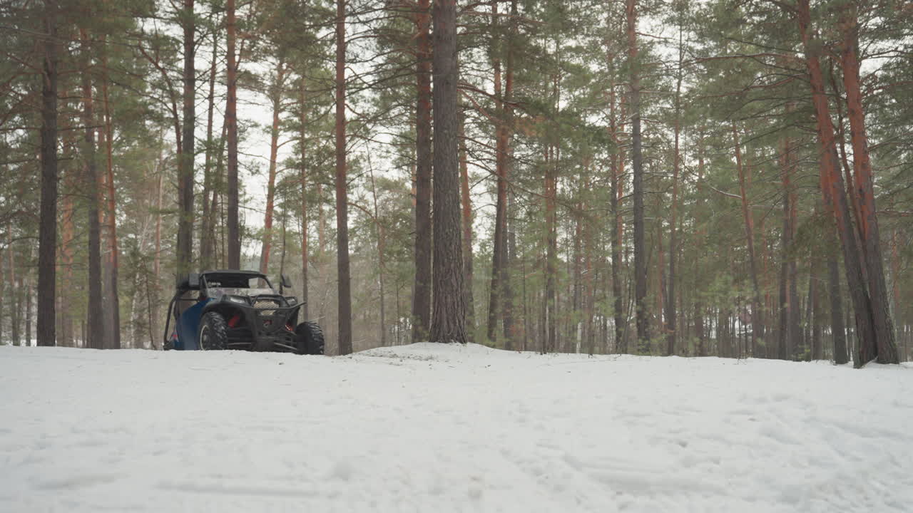 Un UTV blu si fa strada attraverso una foresta di pini innevata. Il conducente naviga su un sentiero ghiacciato tra pini alti, sotto una luce calma e nuvolosa. Ci sono profonde tracce di pneumatici nella neve fresca. È un veicolo fuoristrada robusto, in una solitudine invernale cinematografica.