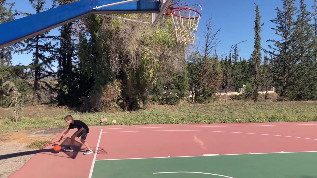 Un giovane ragazzo palleggia con un pallone da basket su un campo all'aperto a Kifisia, Grecia
