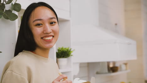 happy japanese girl eating takeaway ramen while looking at the camera and smiling 2