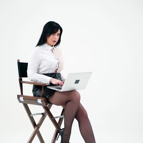 business woman starts working on a laptop in studio. attractive brunette in blouse and skirt sitting alone with modern gadget on white background. freelance concept.