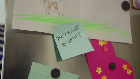 A-man-opens-a-refrigerator-door-with-a-reminder-on-it,-"Don't-forget-to-vote"