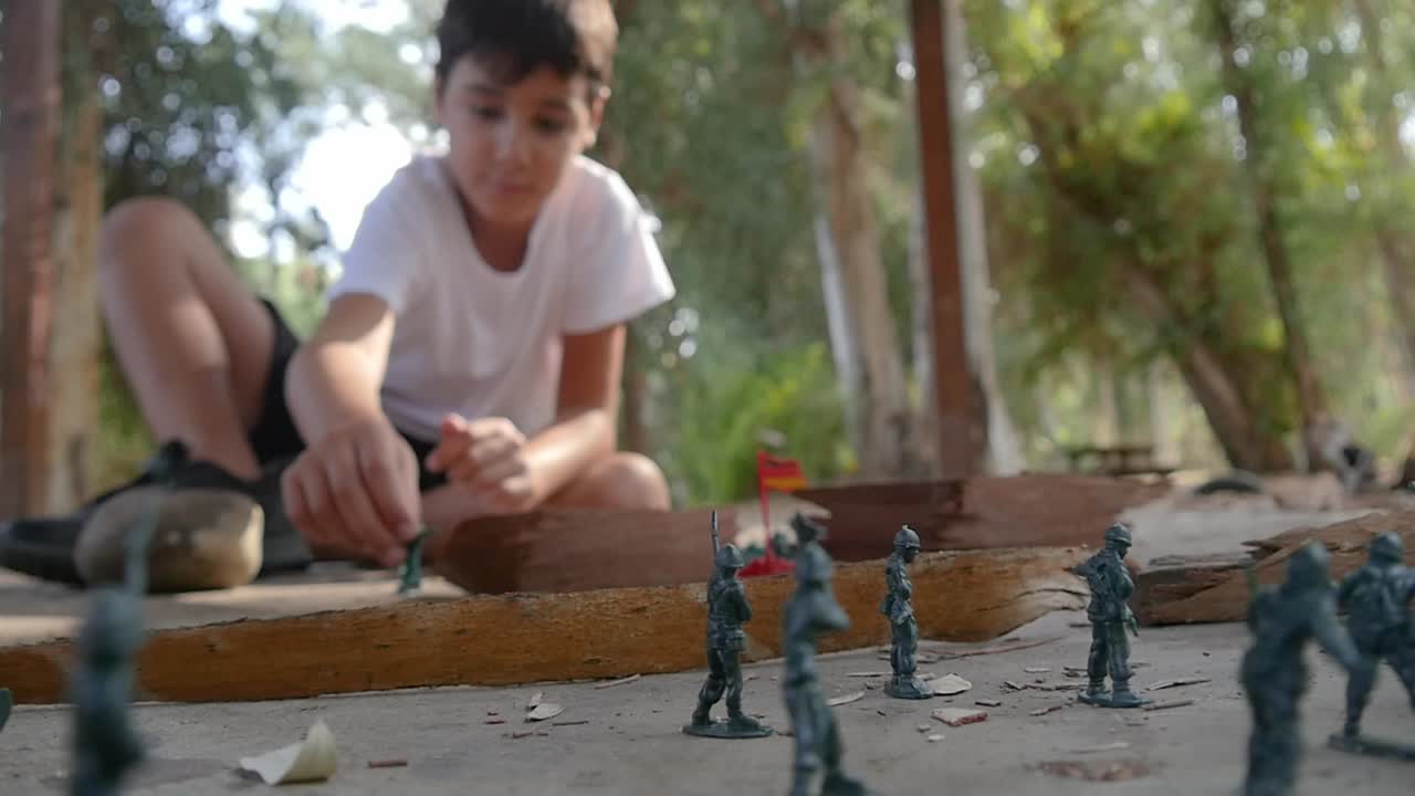 un niño juega solo con hombres del ejército verde de plástico en el parque
