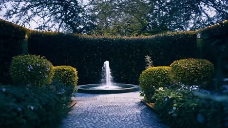 camera gliding toward a beautiful water fountain nestled in a lush garden, surrounded by vibrant flowers and greenery