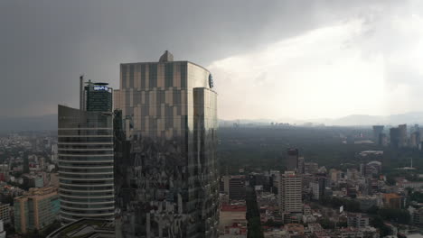Die-Drohnenkamera-Steigt-Und-Fliegt-In-Richtung-Eines-Modernen-Bürogebäudes-Aus-Glas.-Dramatischer-Bewölkter-Himmel-Vor-Starkem-Regen.-Mexiko-Stadt,-Mexiko.