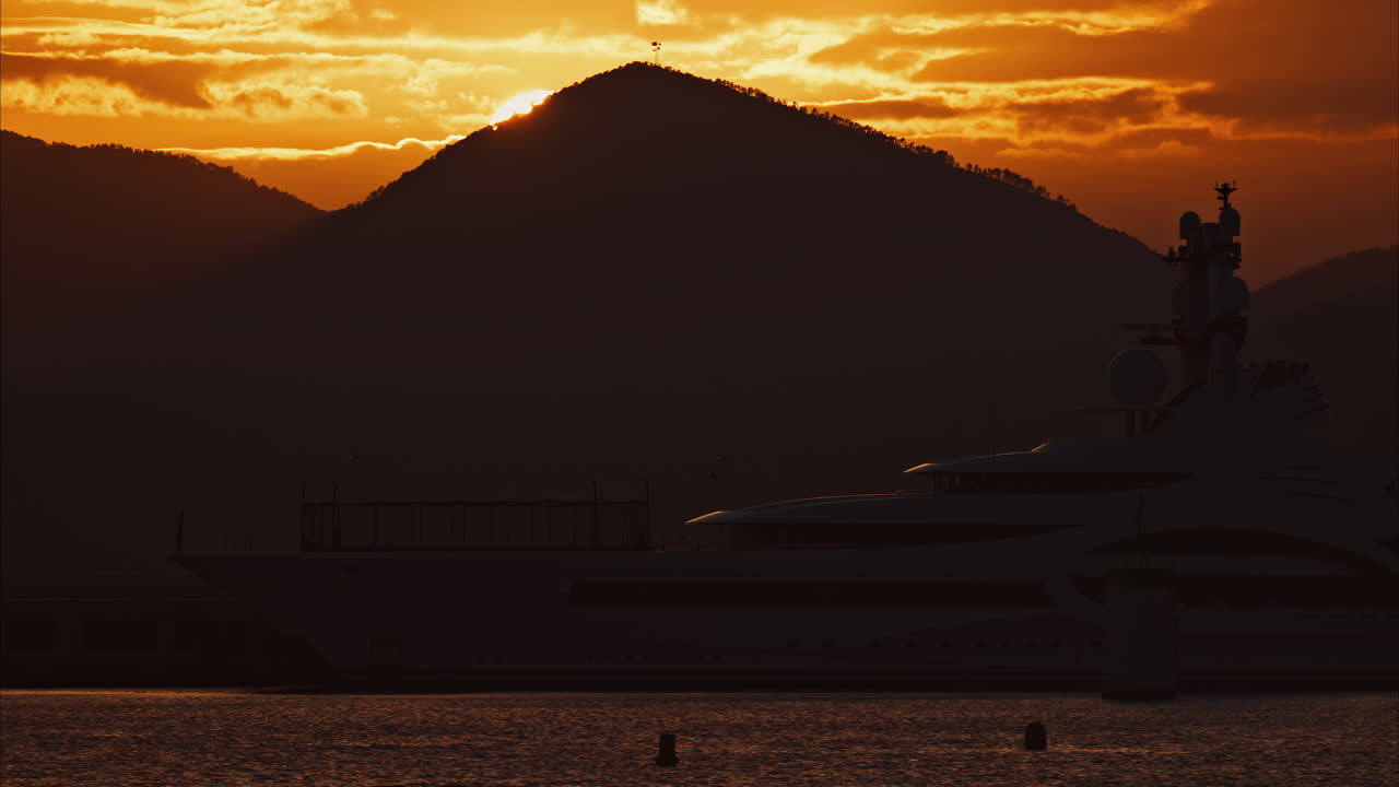 Distant view of a yacht docked on the sea with a mountain on the background at sunset