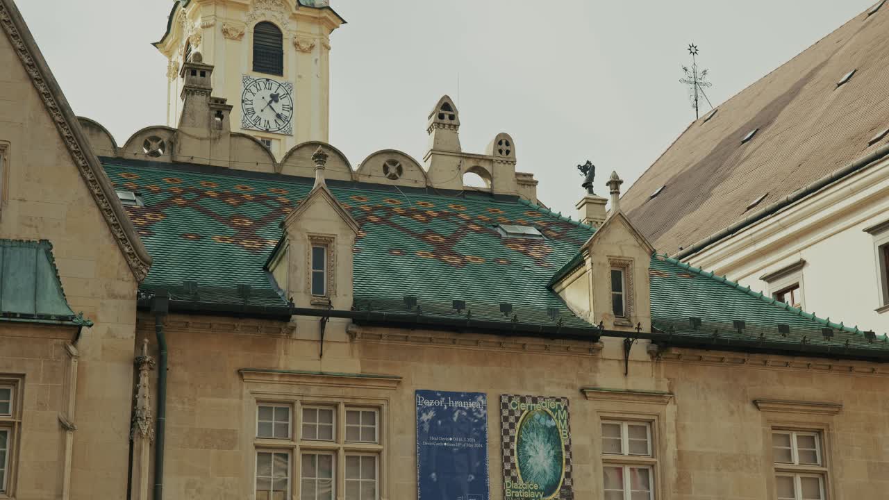 Decorative green roof with colorful patterns and clock tower under a soft European sky