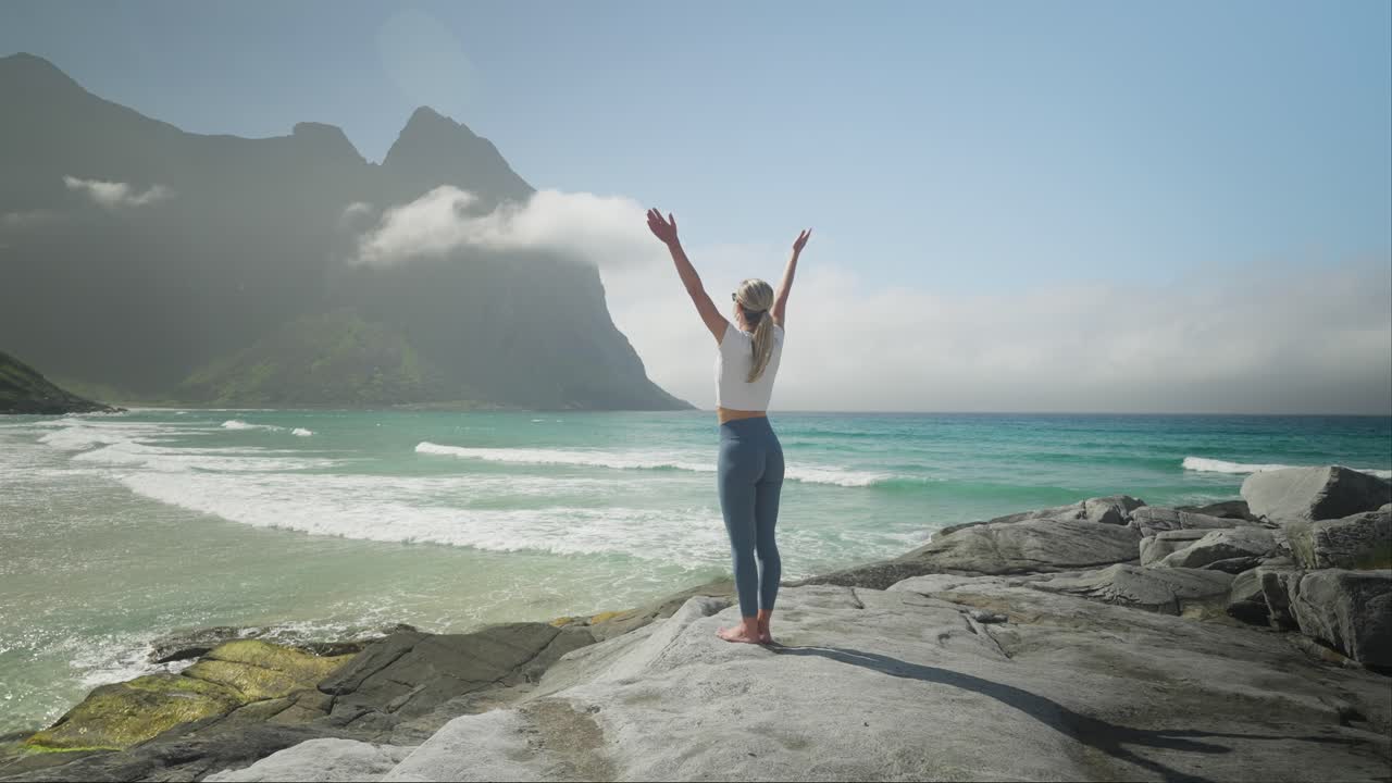 joven delgada practicando yoga en la costa de noruega en un día soleado, vista trasera