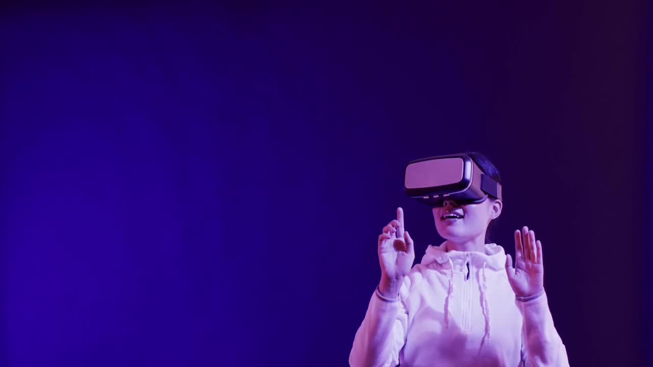 Asian woman using vr headset, touching virtual screen on blue background, copy space, slow motion