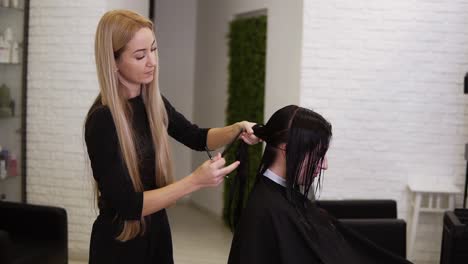 Blonde-Friseurin-Hält-Schere-Und-Kamm-In-Der-Hand-Und-Teilt-Die-Nassen-Haare-Ihrer-Kunden-Für-Einen-Perfekten-Haarschnitt.-Junge-Schöne-Frau-Im-Schönheitssalon-Haare-Schneiden.-Prozess-Des-Haarschneidens-Mit-Einer-Schere.-Seitenansicht.-Zeitlupe