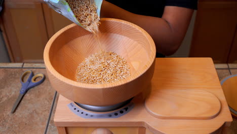 Pouring-Kamut-or-Khorasan-Wheat-into-Wooden-Grain-Mill-Grinder,-Closeup