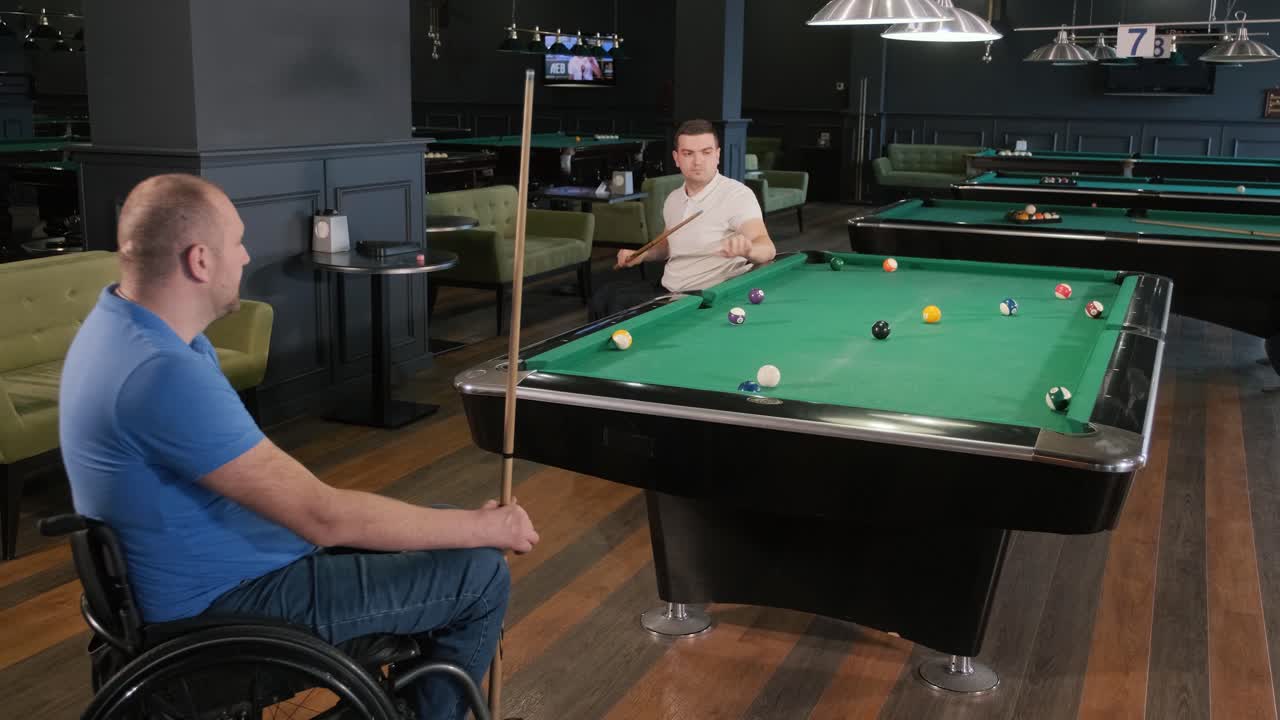 Adult men with disabilities in a wheelchair play billiards in the club