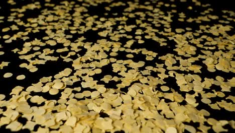 closeup of yellow confetti paper particles fall from above on black table