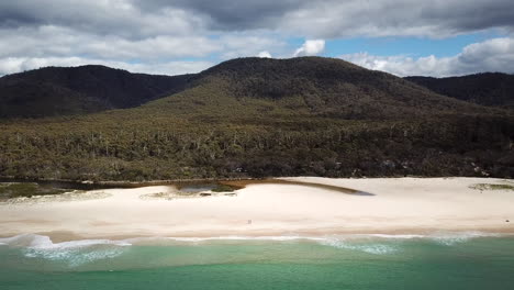 Drone-Pan-Out-From-Two-Isolated-People-On-White-Sand-Beach-With-Waves-Trees,-Tasmania-Australia