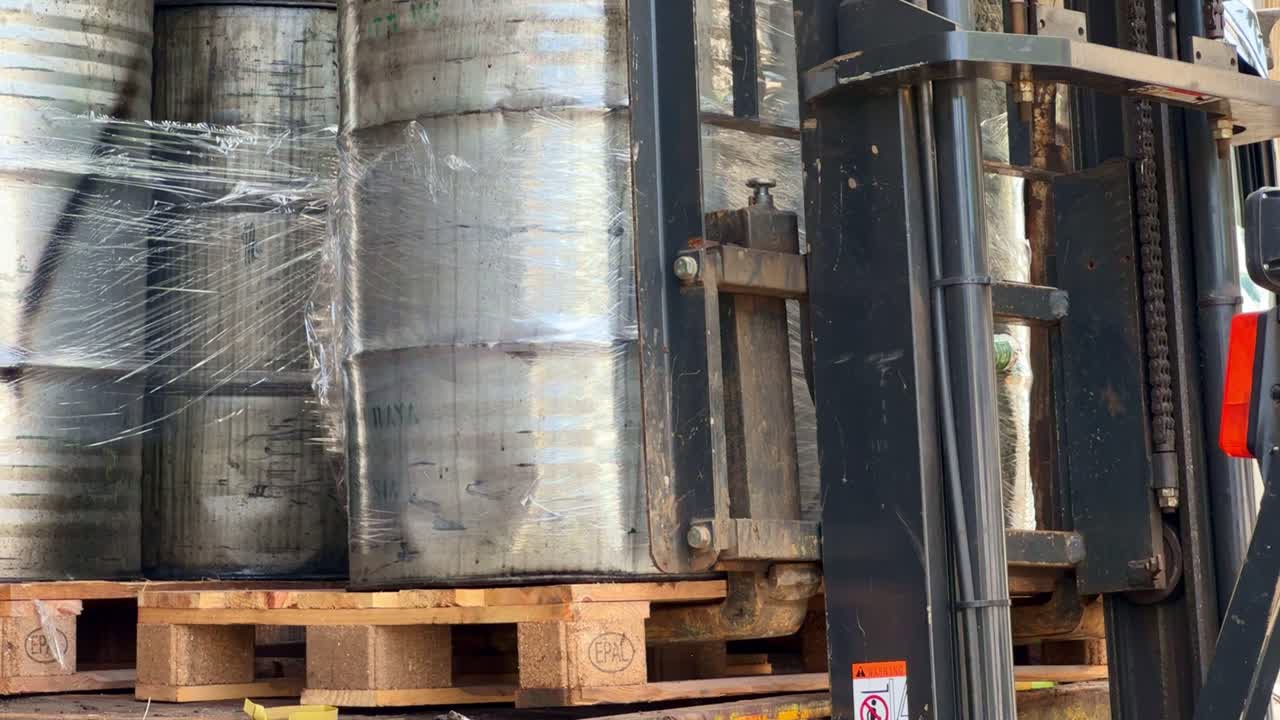 Palletized metal barrels being transported by a forklift in an industrial area